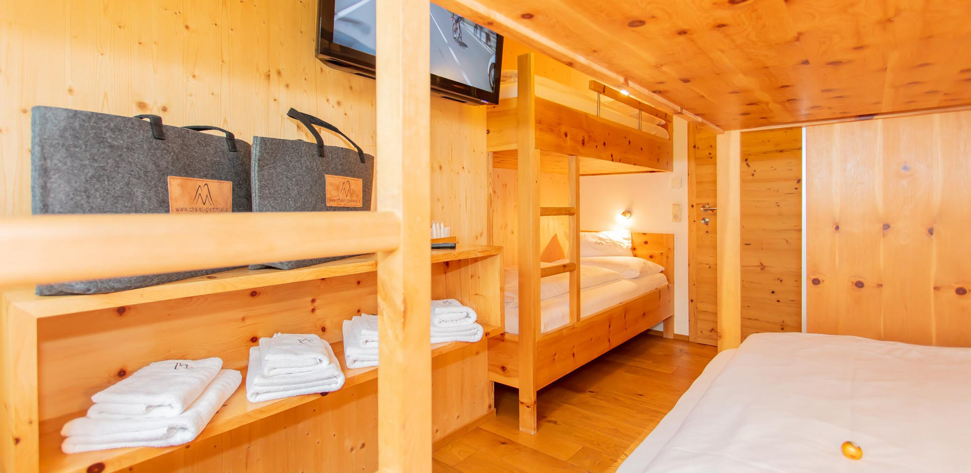 Gemütliches Schlafzimmer in einem Chalet in Saalbach‑Hinterglemm mit Holzwänden und Holzbetten, Etagenbett‑Bettgestell, Handtüchern und TV‑Monitor an der Wand.