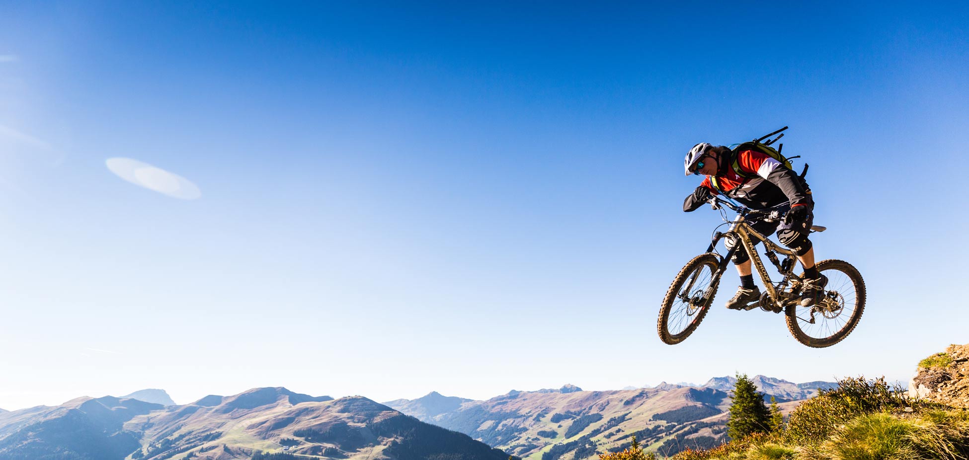 Mountainbiker springt mit Helm und Schutzkleidung vor Berglandschaft