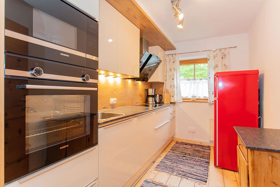 Modern kitchen with built-in Siemens oven and microwave, white cabinets, wooden countertop, red refrigerator, window with floral curtains, and patterned rugs on tiled floor