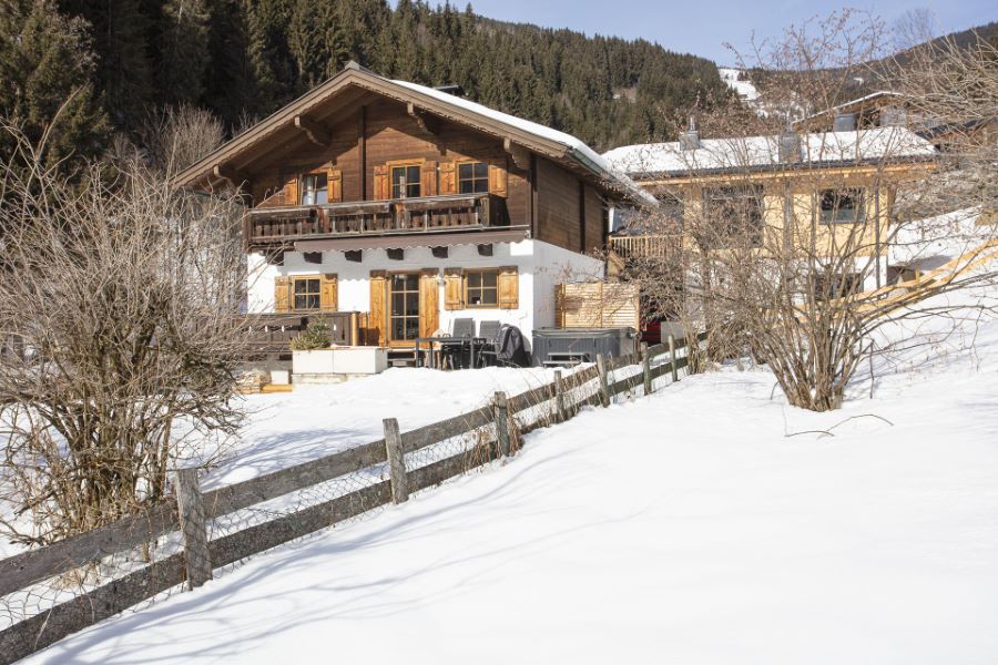 Holz‑Alpenchalet im Winter in Viehhofen/Saalbach‑Hinterglemm mit verschneitem Dach und Umgebung, umgeben von schneebedeckten Bäumen und Bergen im Hintergrund.