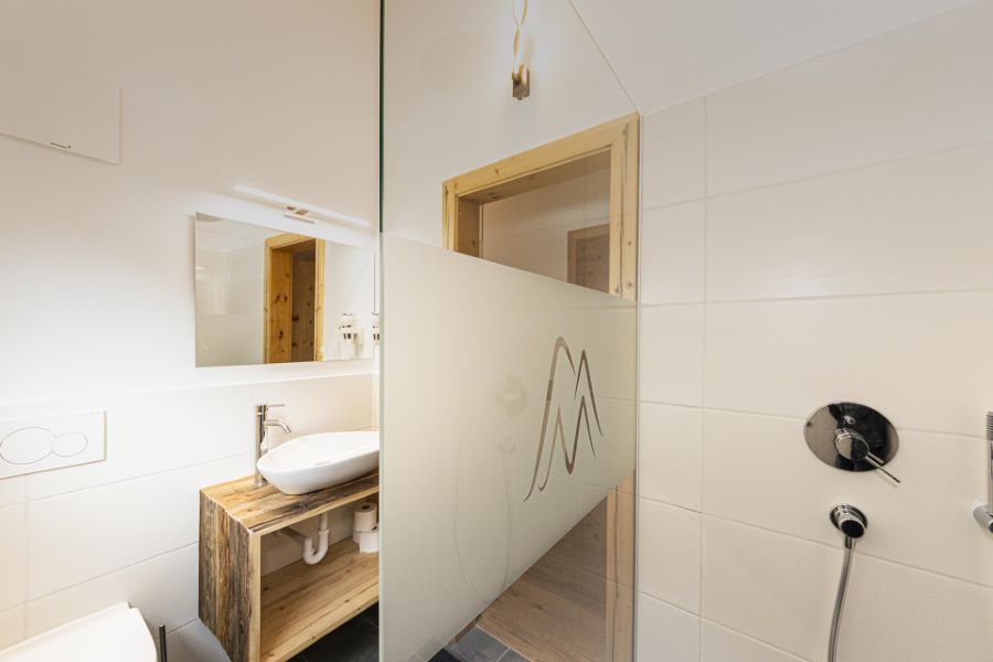 Badezimmer mit Holzwaschtisch, ovalem Aufsatzwaschbecken, Spiegel und halbhoher Glaswand mit Bergmotiv