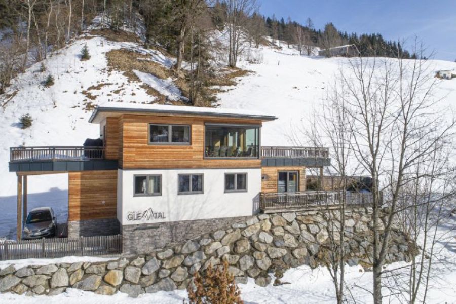 Verschneites Alpen‑Chalet in Viehhofen bei Saalbach‑Hinterglemm im Winter mit schneebedecktem Dach, umgeben von Bäumen und Bergen in der Salzburger Berglandschaft.