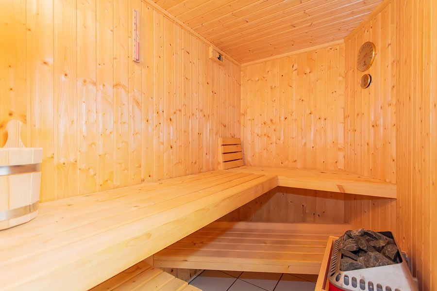 Interior of a wooden sauna with benches, a bucket, and a heater with stones