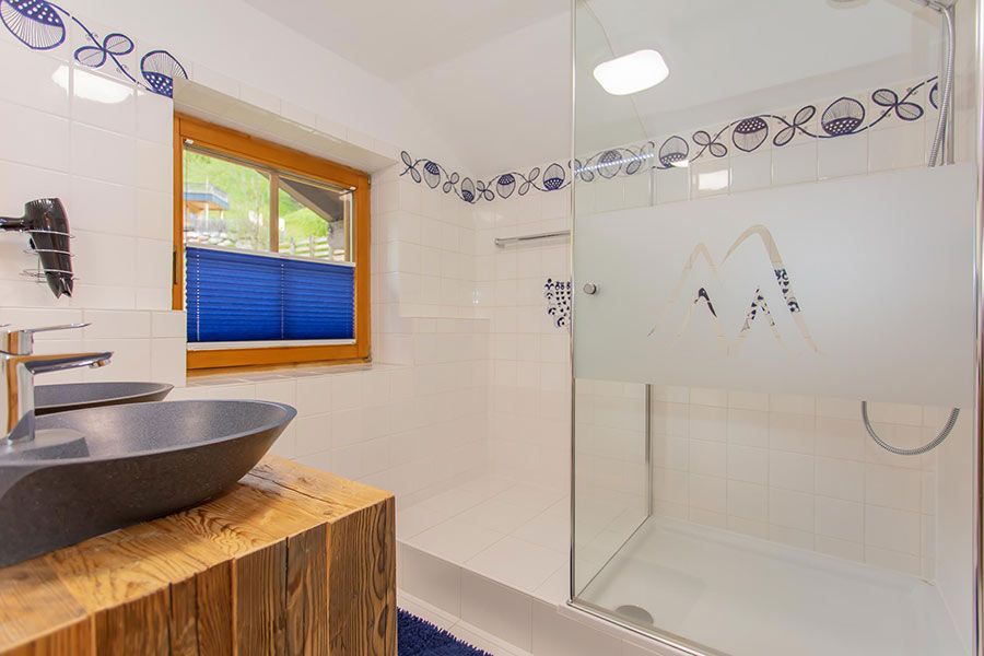 Bathroom with wooden-framed window, blue blinds, stone vessel sink on wooden countertop, and glass shower enclosure with frosted design