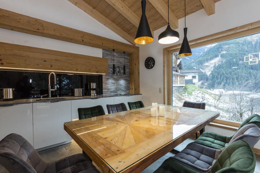 Essbereich mit großem Holztisch, gepolsterten Stühlen, moderner Küche und großem Fenster mit Bergblick