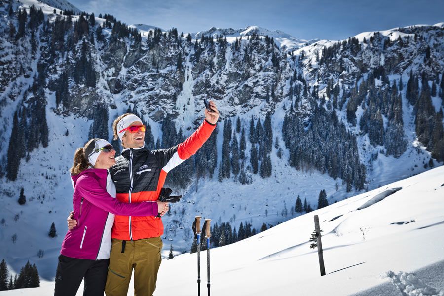 Zwei Personen in Winterkleidung machen vor schneebedeckten Bergen ein Selfie