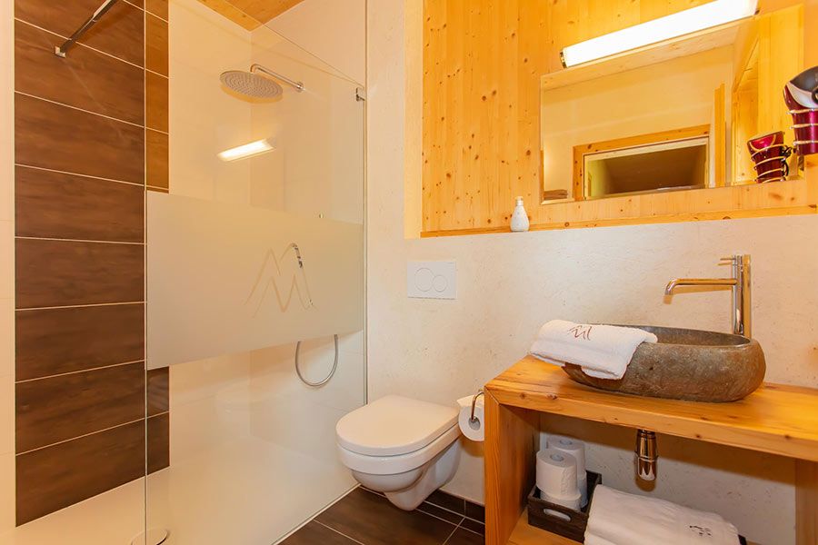 Kleines Badezimmer mit Holzverkleidung, Wand-WC, Steinwaschbecken auf Holzablage und begehbarer Dusche mit Glasabtrennung