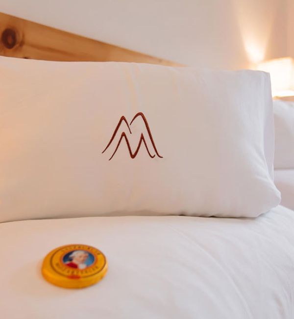 Zwei weiße Kissen mit braunem Berg-Logo auf einem Bett mit weißer Bettwäsche