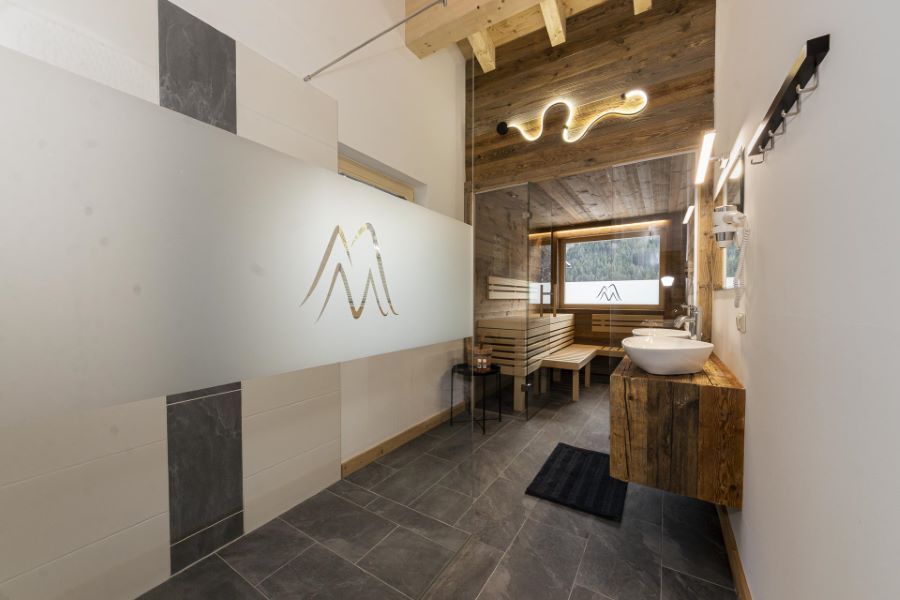 Moderner Wellnessbereich mit Sauna, Holzverkleidung, zwei Waschbecken auf Holzkonsole und großem Fenster mit Bergblick