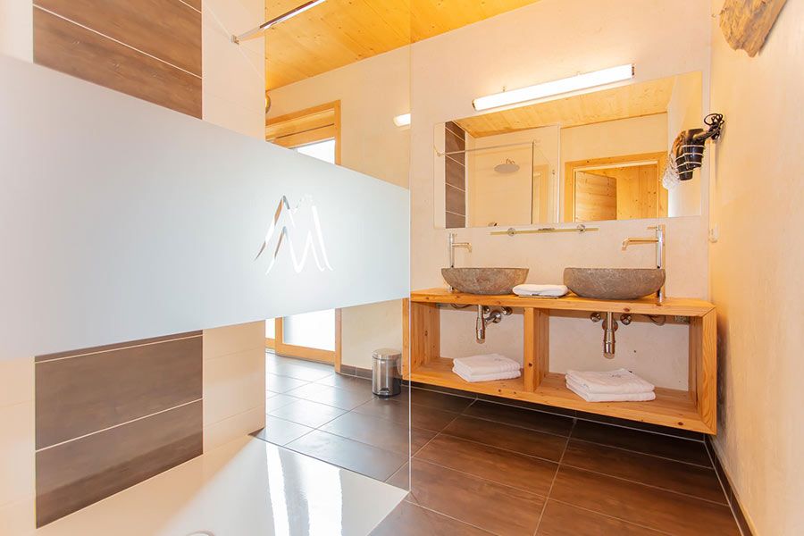 Badezimmer mit zwei steinernen Waschbecken auf Holzregal, großem Spiegel und teilverglaster Duschkabine