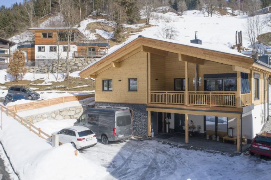 Verschneite Winterlandschaft mit einem traditionellen Holz‑Chalet in Viehhofen bei Saalbach‑Hinterglemm, Österreich, umgeben von tiefem Schnee, Nadelbäumen und Bergen im Hintergrund.