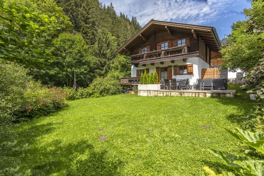 Rustikales Chalet in den Alpen des Glemmtals bei Saalbach‑Hinterglemm/Viehhofen im grünen Sommer mit Holzfassade, Balkon und Bergwald im Hintergrund.