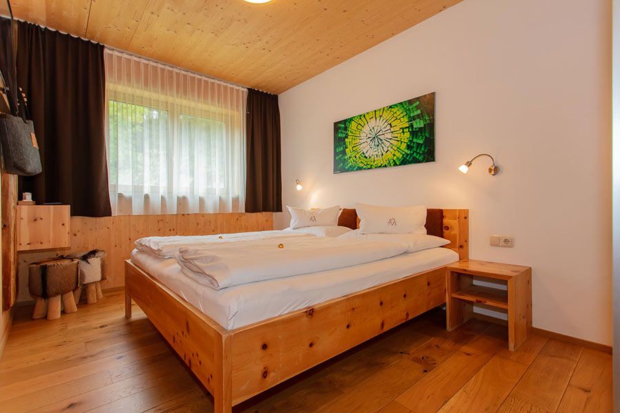 Schlafzimmer mit Holzbett, Holzboden, Nachttisch, großem Fenster mit Vorhängen und abstraktem Bild an der Wand