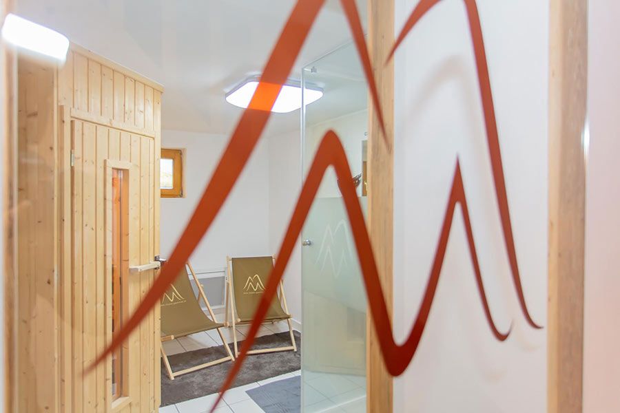 Room with wooden sauna door, two folding chairs with mountain logos, and a glass shower door with red mountain-shaped decals