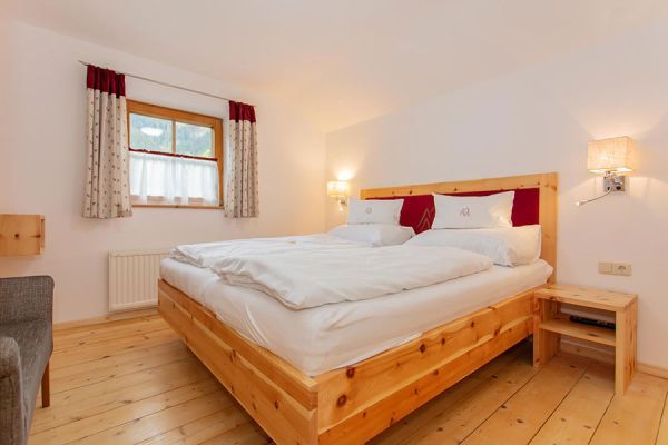 Hell eingerichtetes Schlafzimmer mit Holzbett, Holzboden, Fenster mit gemusterten Vorhängen und zwei Wandlampen